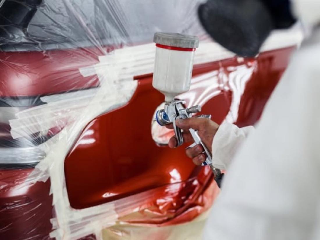 Technician spraying red paint on a panel